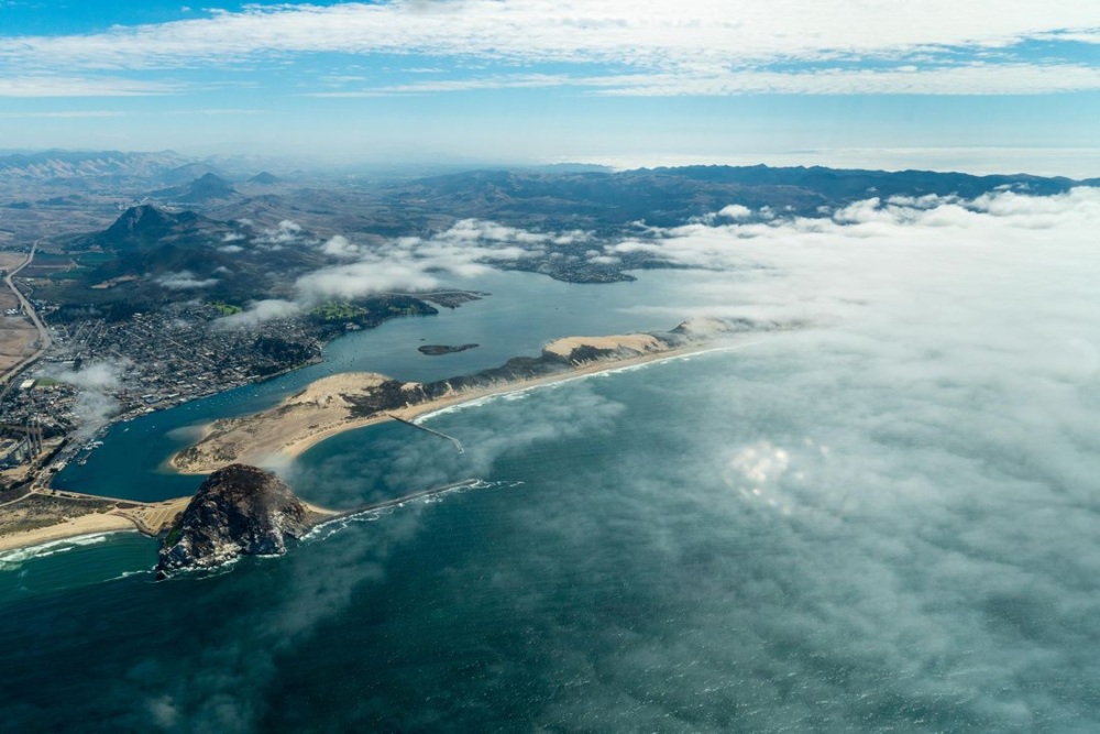 Aerial view of a Pacific shoreline with the mound of Morro Rock sitting just off the coastline.